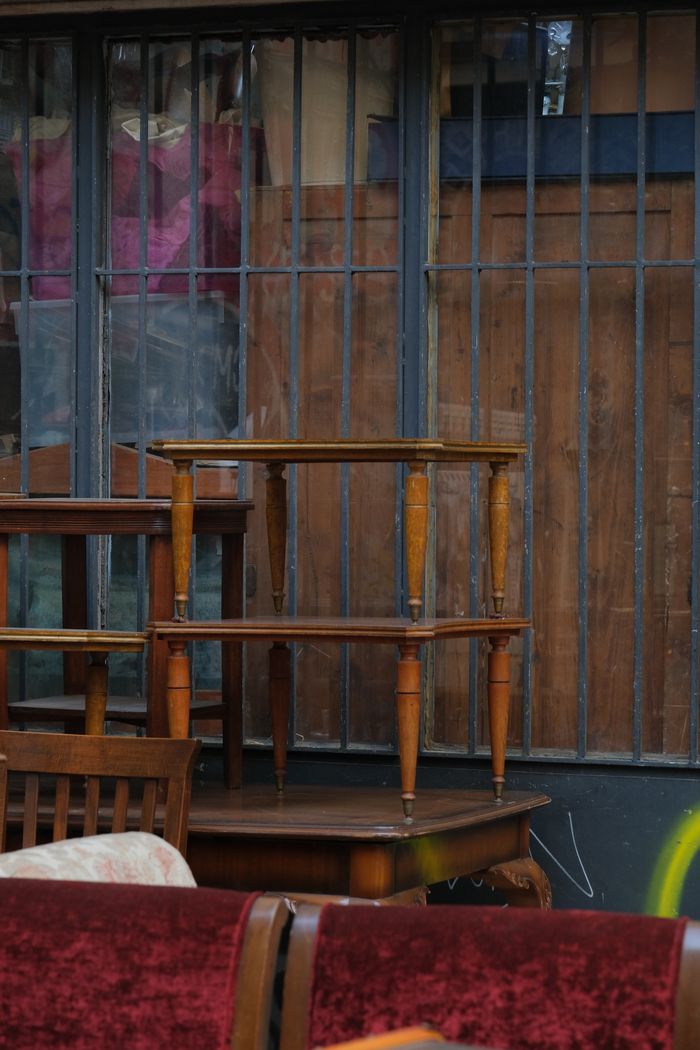 Stack of vintage wooden tables and chairs against a rustic wall in an urban environment.